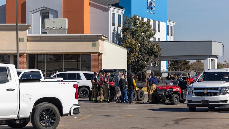 Business owners and first responders gather in a shopping center parking lot near the scene of...